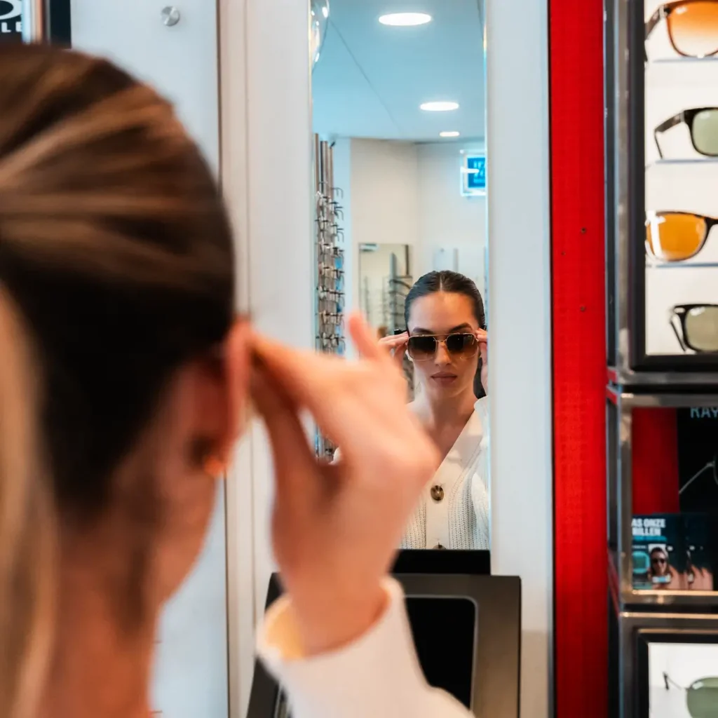 Vrouw past een Ray-Ban zonnebril voor de spiegel in de winkel van Teeling Amsterdam